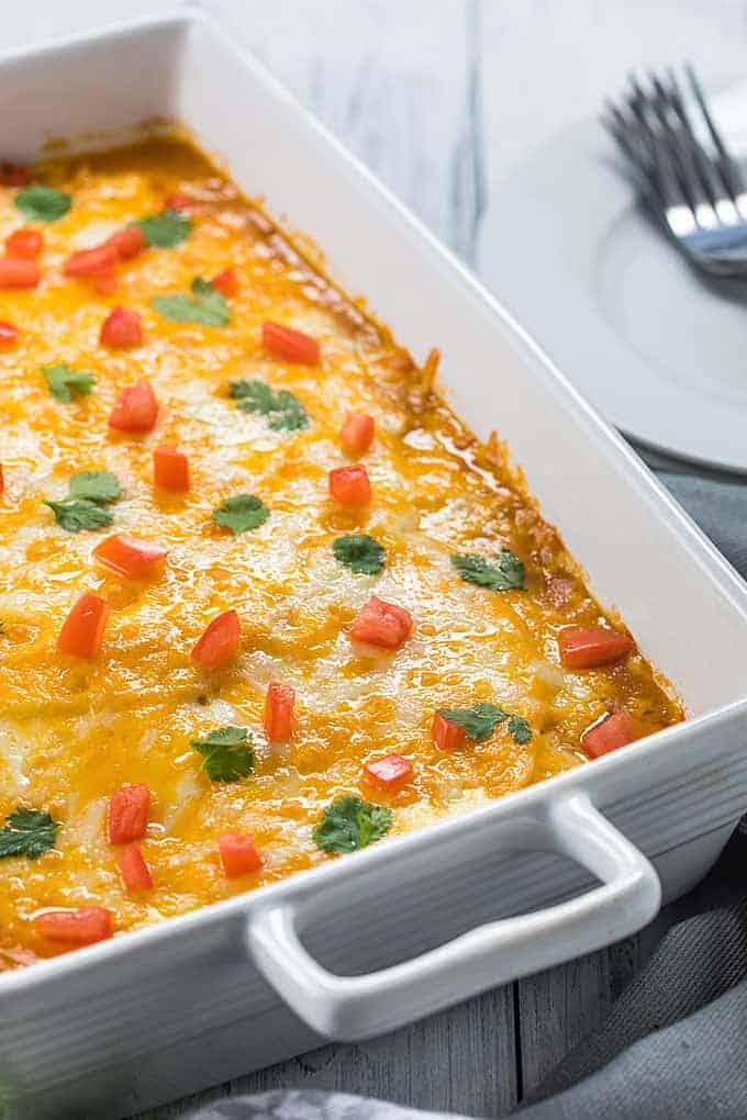A casserole topped with cheese, tomatoes and cilantro in a white baking dish.