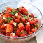 Watermelon Feta Salad with mint in a clear glass bowl beside a white cloth napkin