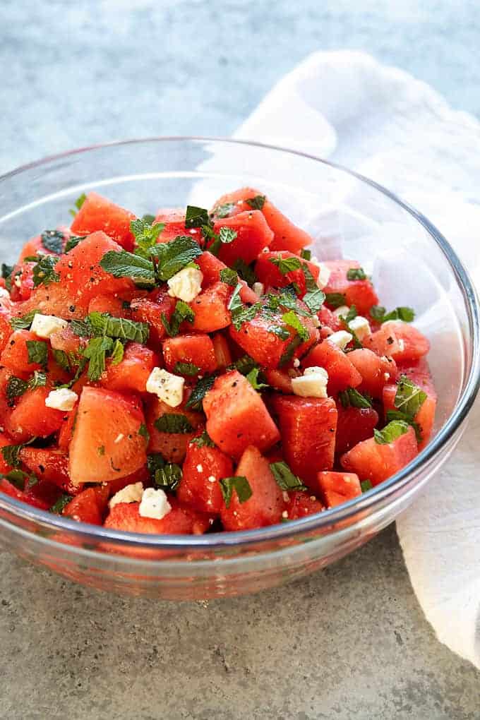 Watermelon Feta Salad with mint in a clear glass bowl beside a white cloth napkin.