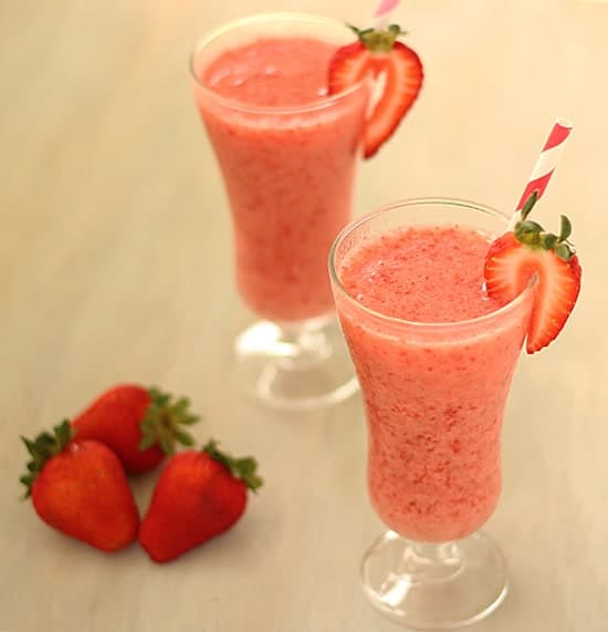 Two frozen strawberry drinks with straws garnished with fresh strawberries.