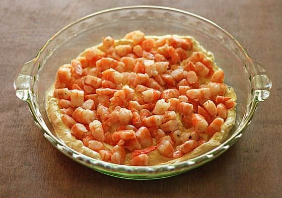 A round clear glass dish with chopped cooked shrimp on top of a cream cheese mixture.