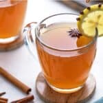 Hot toddy in a glass mug garnished with lemon and star anise. Overlay text at top of image.