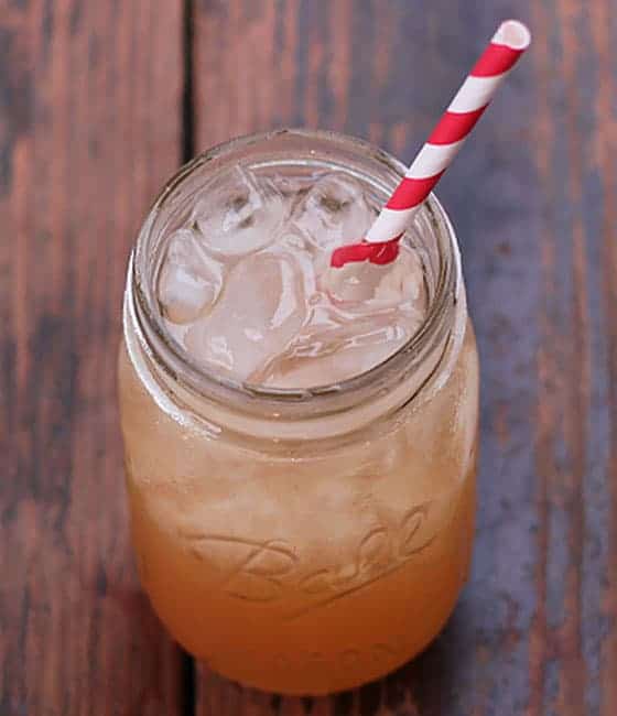 An apple cider cocktail in a mason jar with a red and white striped straw.
