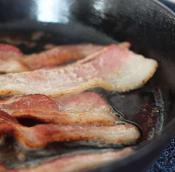 A closeup of bacon frying in a cast iron skillet.
