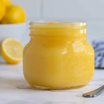 A jar of lemon curd with a bowl of lemons in the background.