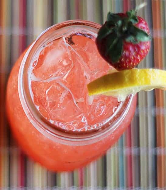 Overhead view of an iced strawberry lemonade cocktail in a mason jar.