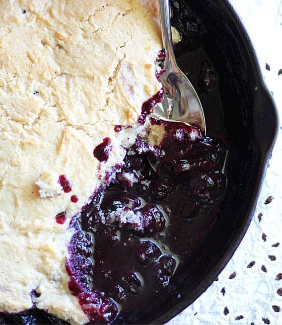 Overhead view of blueberry cobbler in a skillet with a spoon.