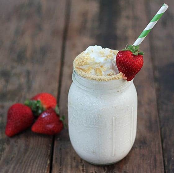 A milkshake in a jar with a green striped straw and garnished with a fresh strawberry.