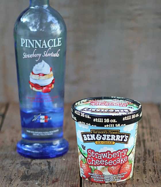 A pint of strawberry cheesecake ice cream and a blue bottle of vodka on a wood surface.