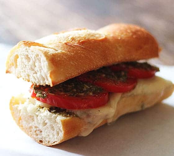 A toasted baguette with sliced tomatoes, pesto and cheese.