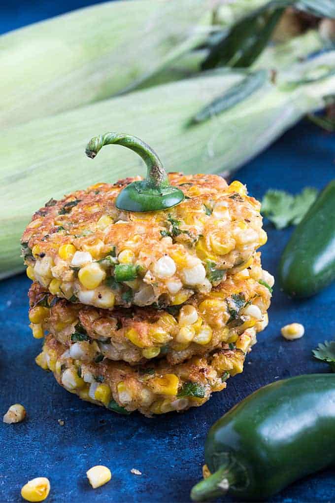 A closeup view of three stacked jalapeno corn fritters on a blue surface.