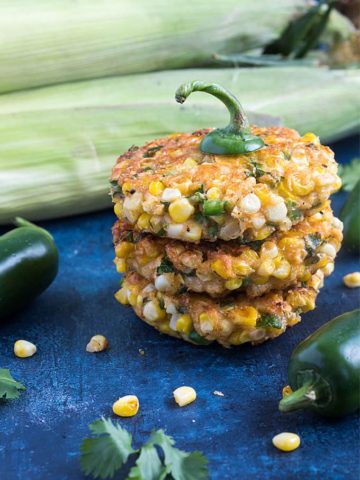 Three stacked corn fritters with a jalapeno stem on top on a blue surface.