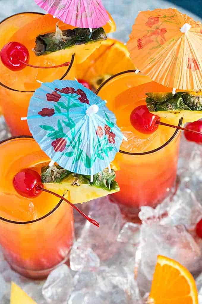 Overhead view of three orange cocktails garnished with fruit and umbrellas.