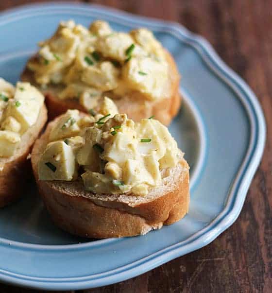 Sliced French bread spread with egg salad on a blue plate.