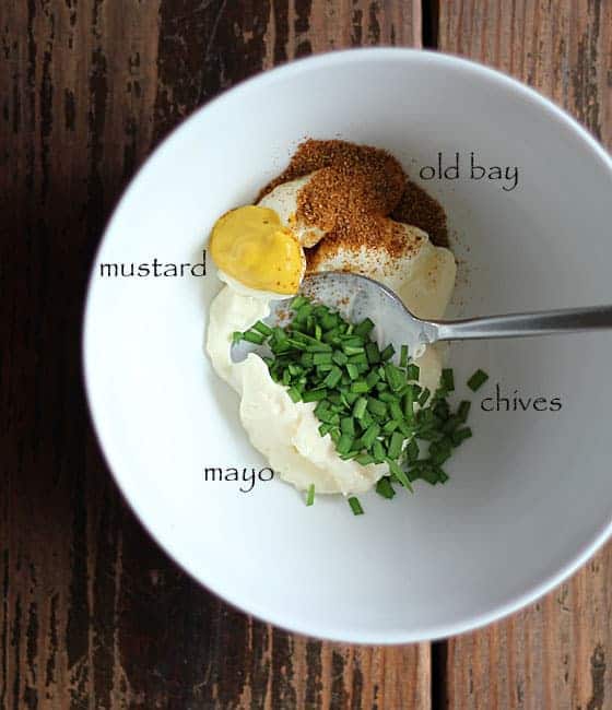 Mustard, seasoning, chives and mayonnaise in a shallow bowl with a spoon.