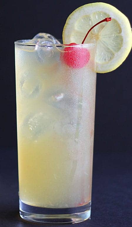 A closeup of a lemonade cocktail garnished with a cherry and lemon slice.