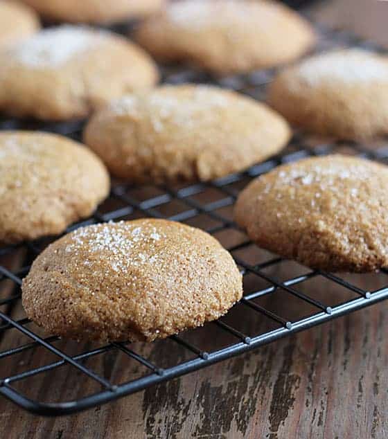 A closeup of gingersnap cookies on a wire baking rack on a wood surface.