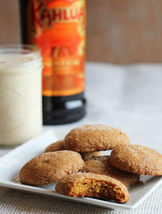 Gingersnap cookies on a square white plate. A glass of milk and bottle of liqueur is in the background.