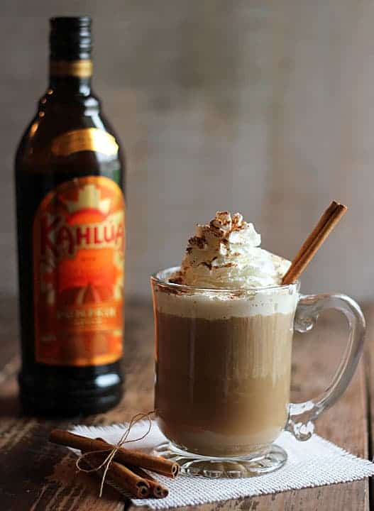 A coffee cocktail topped with whipped cream.  A bottle of liqueur is in the background.
