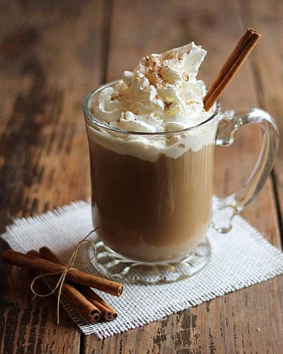 A coffee cocktail in a clear glass mug topped with whipped cream and a cinnamon stick.