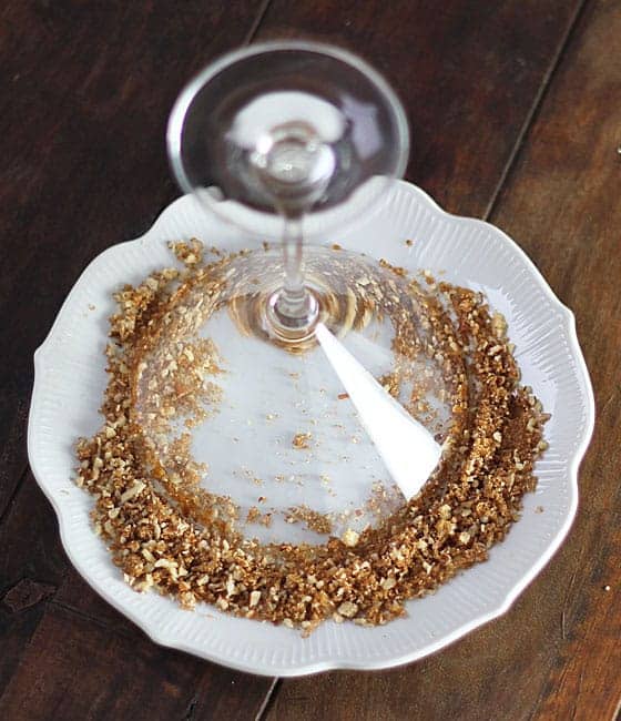 A martini glass turned upside-down into crushed pecans and brown sugar on a white plate.