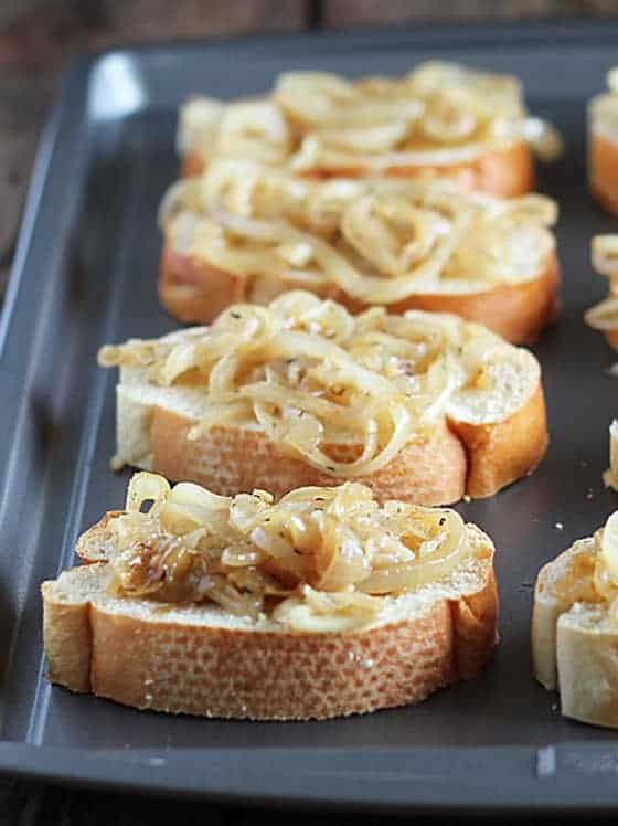 Slices of french bread topped with cooked onions on a baking sheet.