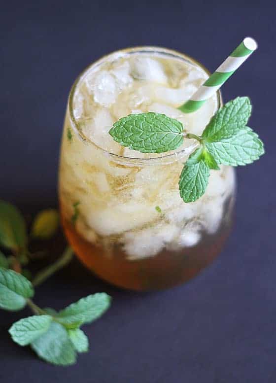 A mint julep cocktail in a glass with a green striped straw on a black background.