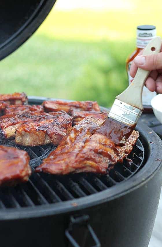 Ribs being basted with barbecue sauce on an outdoor grill.