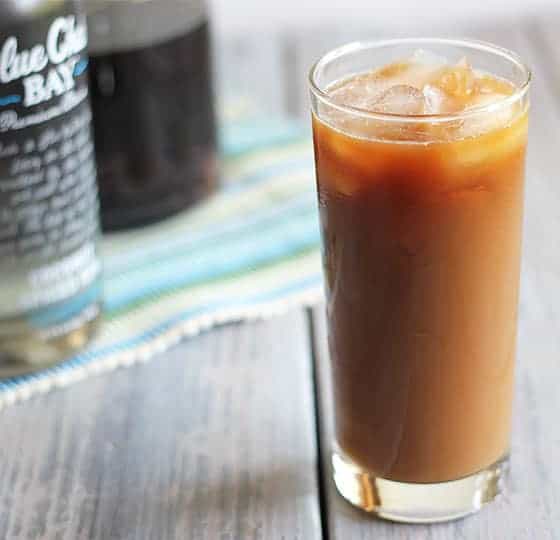 Iced coffee with rum in a glass on a light wooden surface.