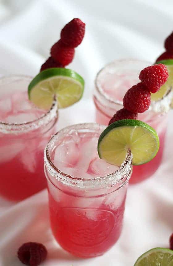 Overhead view of 3 garnished raspberry beer margaritas on a white background.