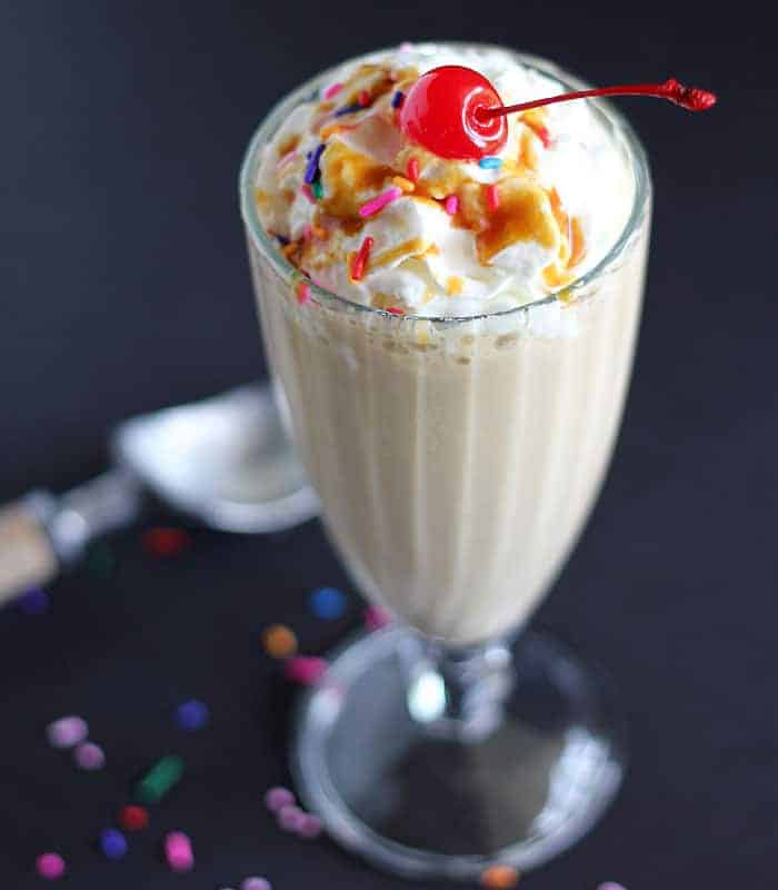 A milkshake prepared with iced coffee, ice cream and banana topped with whipped cream and a cherry.