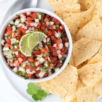 Overhead shot of Pico de Gallo in a round white bowl on a round white plate with tortilla chips.