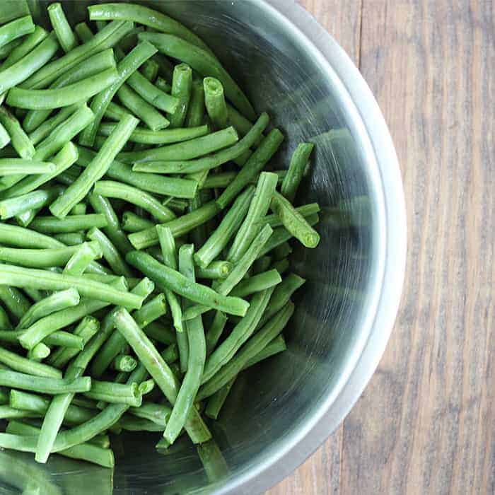 Overhead view of fresh green beans with the ends trimmed in a metal bowl.