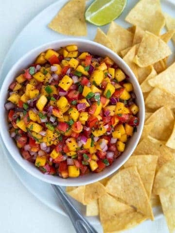 Overhead view of peach salsa in a white bowl on a white plate with tortilla chips