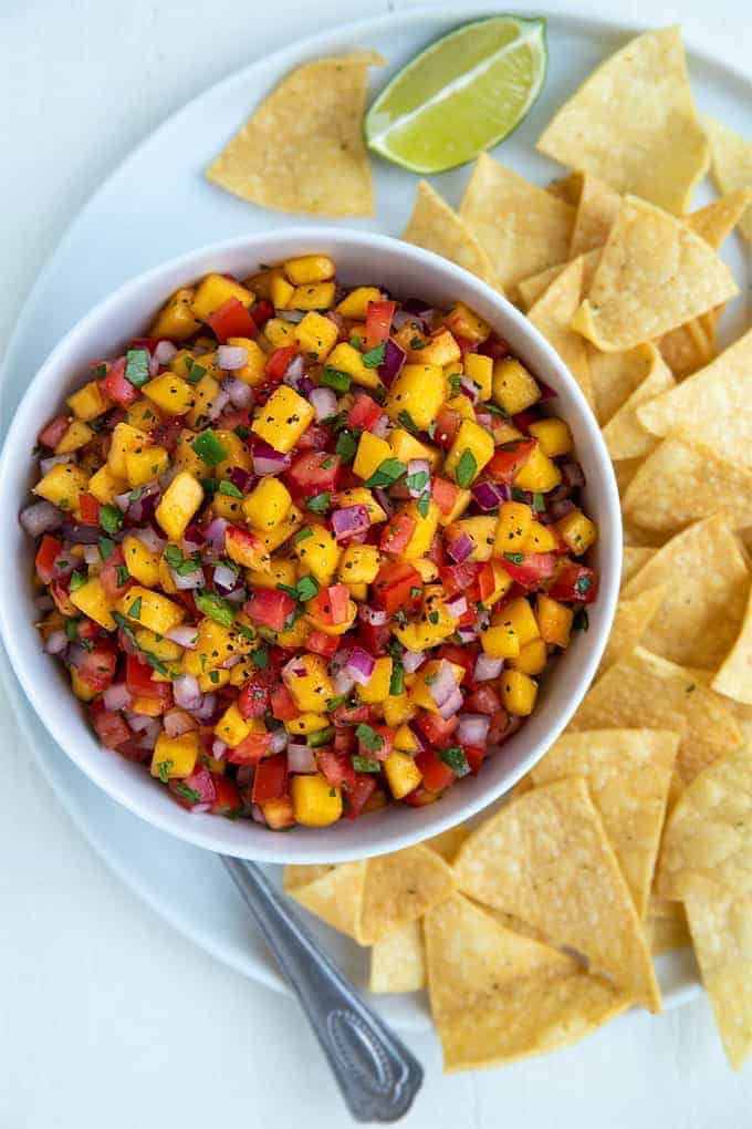 Overhead view of peach salsa in a white bowl on a plate with tortilla chips.