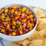Salsa in a white bowl on a plate with tortilla chips. Overlay text reads "peach salsa".