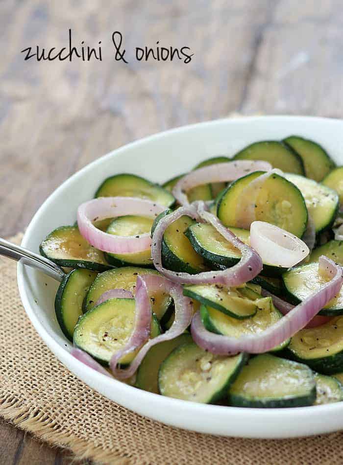 Sauteed zucchini and red onions in a white bowl on a piece of burlap.