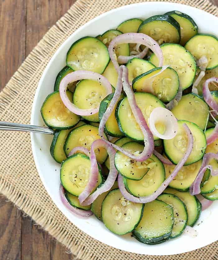 Overhead view of zucchini and onions in a white bowl with a spoon.
