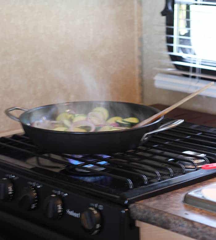 Zucchini squash and onions cooking in a skillet on a small stove in a camper.