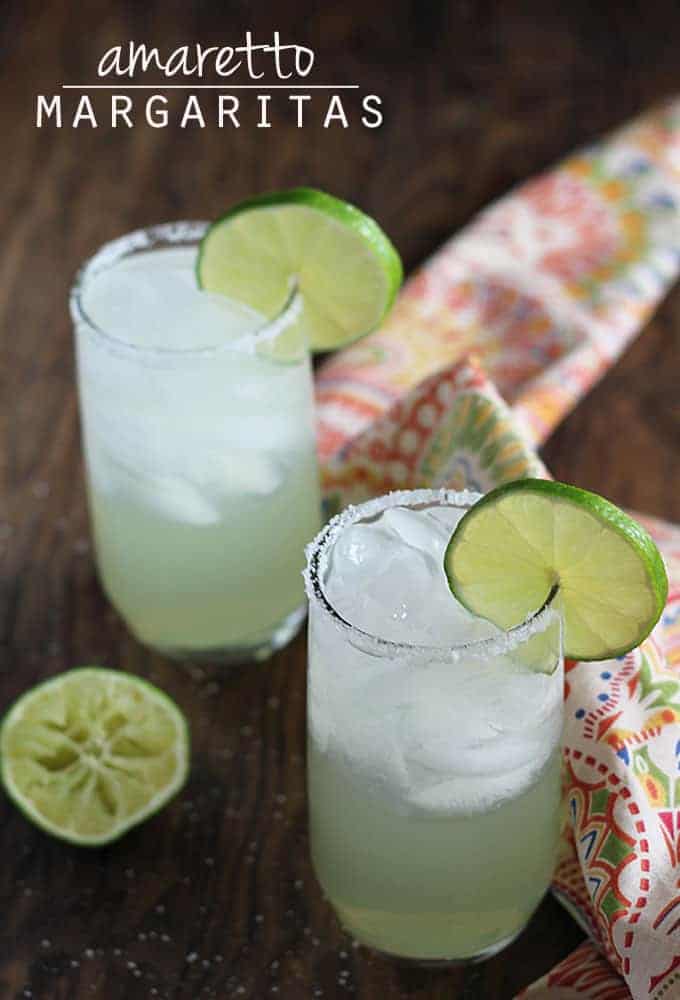 Two margaritas by a squeezed lime and a patterned napkin on a wood background.