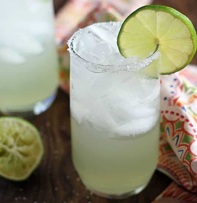 Front closeup view of a margarita in a glass rimmed with salt and garnished with lime.