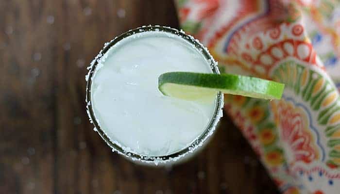 Overhead view of a margarita garnished with a lime wheel by a patterned napkin.