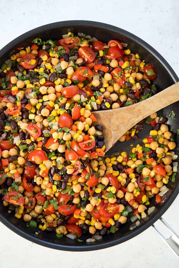 Overhead shot of Southwestern succotash in a large skillet with a wooden spoon.