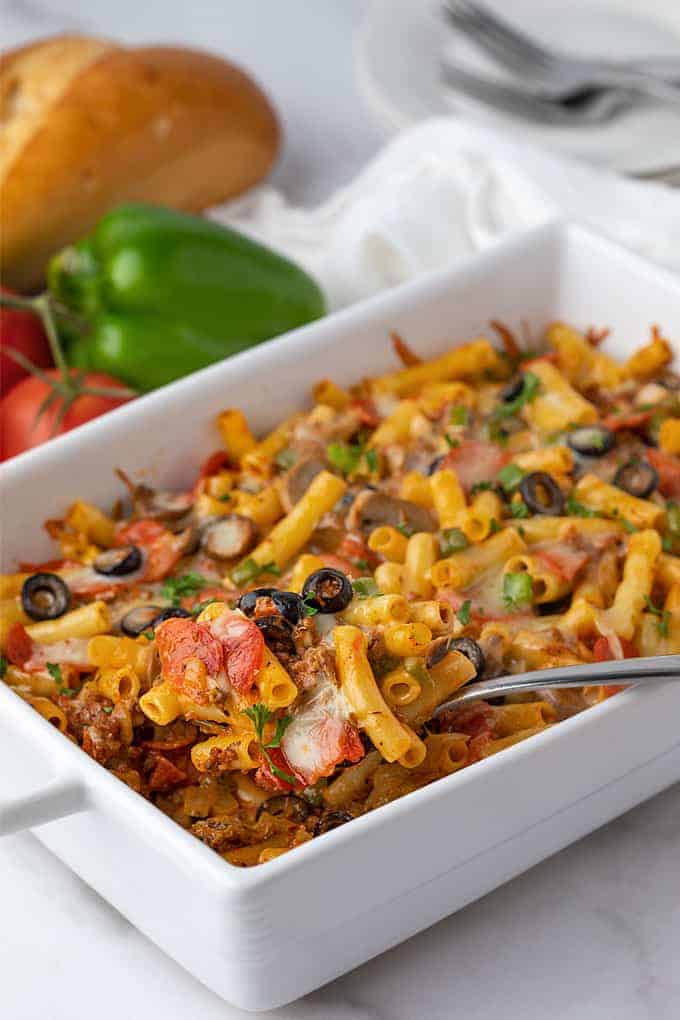 Pizza pasta casserole in a white baking dish with a serving spoon.