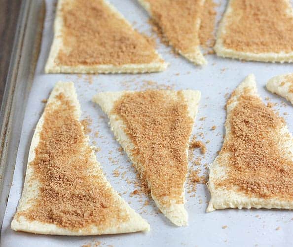 Crescent roll triangles on a baking sheet sprinkled with a brown sugar mixture.