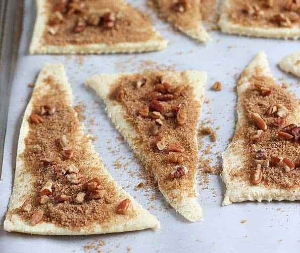 Crescent roll triangles sprinkled with a brown sugar mixture and pecans on a baking sheet.