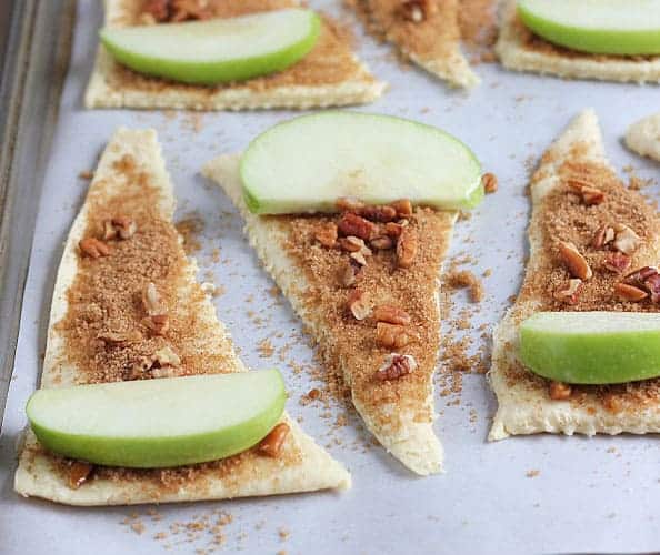 Crescent roll triangles with sugar, spices, pecans and a slice of apple on a baking sheet.