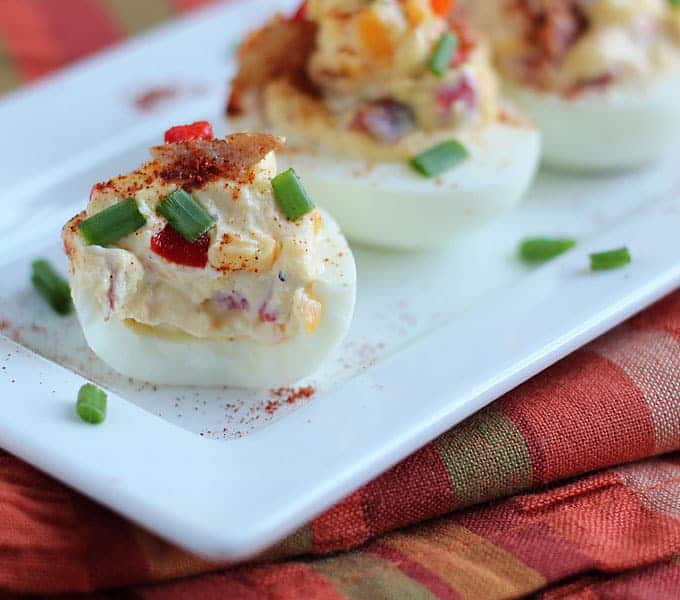 Closeup view of a deviled egg on a white rectangle platter over a striped napkin.