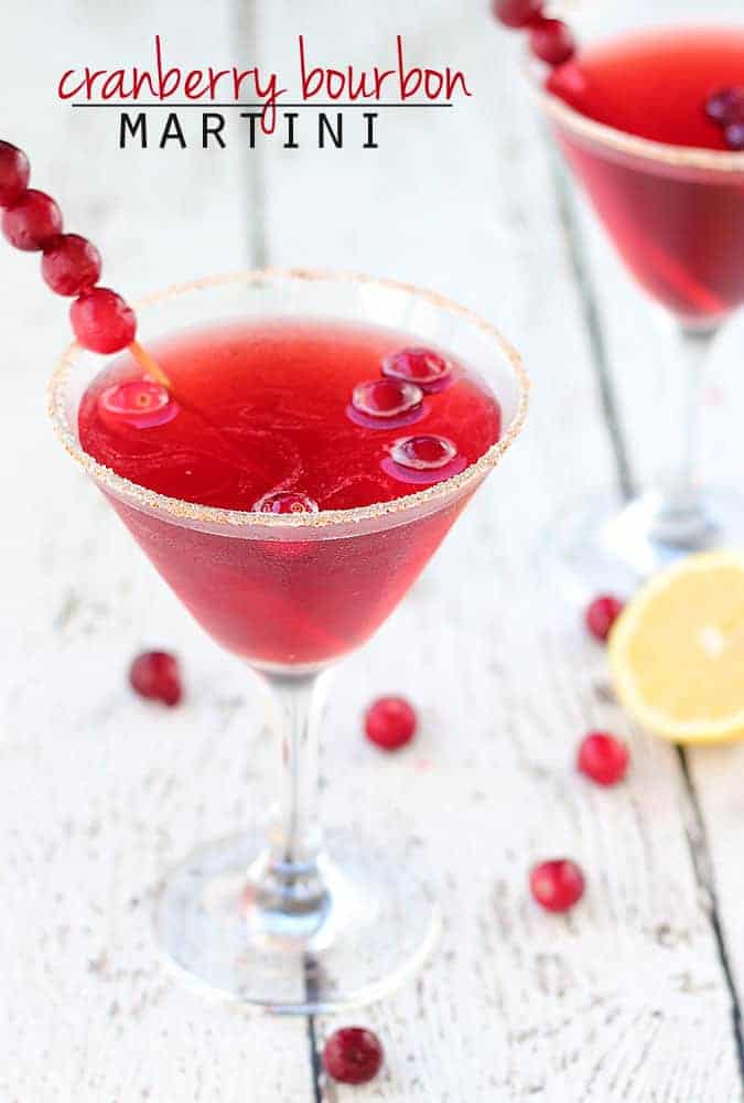 A martini garnished with fresh cranberries on a skewer on a white wood surface.