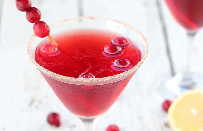 Closeup view of a martini with cranberries in a glass rimmed with nutmeg and sugar.